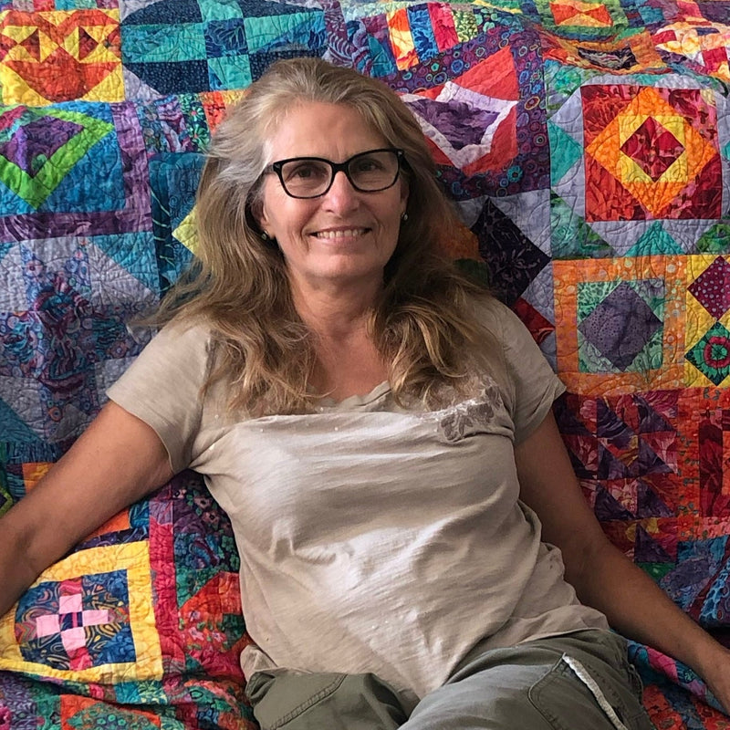Berni Sydow sitting on a colorful quilt with a pattern of geometric shapes.
